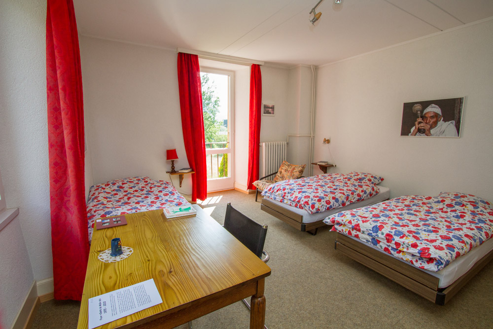 Chambre double du Foyer — deux lits, rideaux rouges, bureau et lumière naturelle