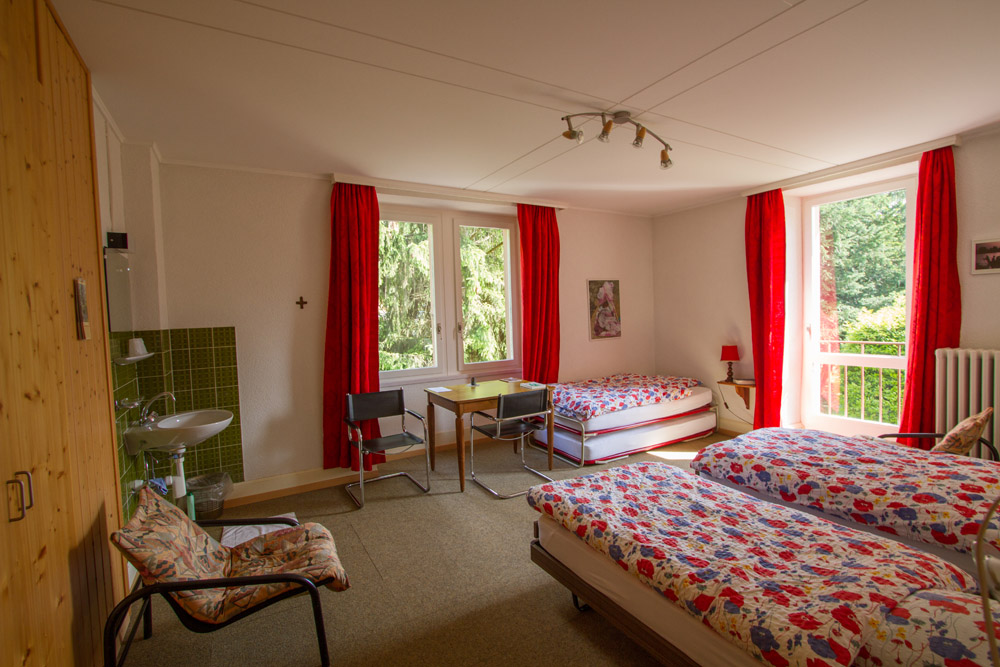 Grande chambre familiale du Foyer — plusieurs lits, lavabo, deux fenêtres avec vue sur les arbres