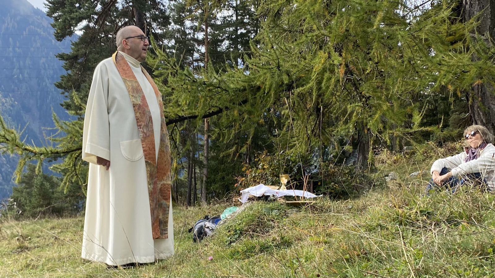Célébration eucharistique en plein air sur un alpage, prêtre et retraitants face aux montagnes