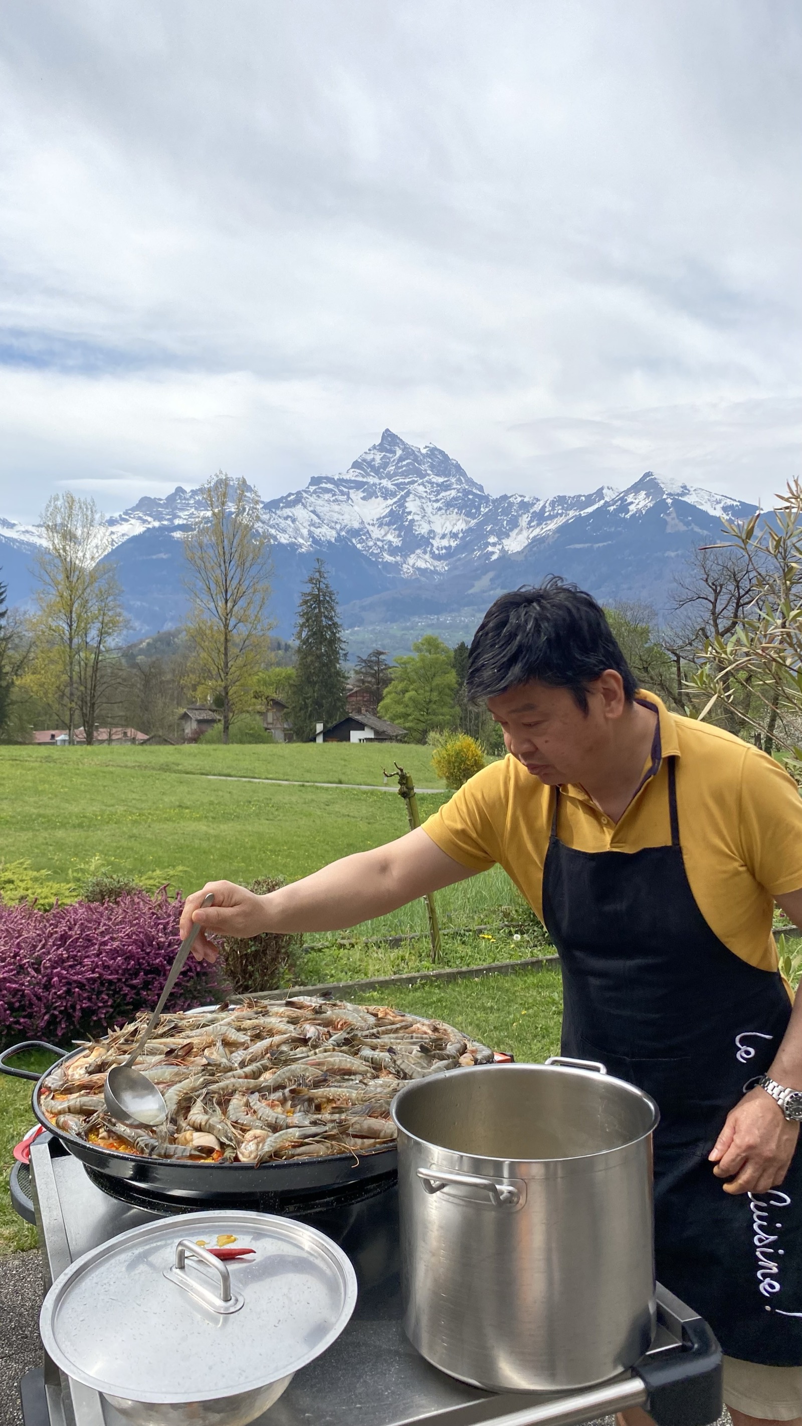 Le cuisinier du Foyer prépare une paella en plein air, avec les Dents-du-Midi en arrière-plan